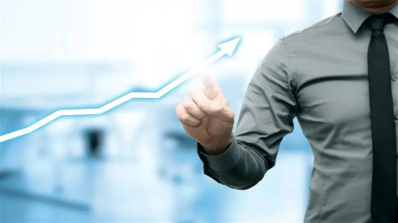 A man in a business shirt points with his finger at a glowing, ascending diagram arrow, symbolizing growth, progress, and success. This image illustrates the concept of business development, positive trends, or performance improvement, often in the context of technological innovations or corporate strategies like those of Origify, aiming for growth and enhancement.