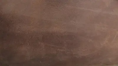 An image depicting a seamless transition or comparison on a dark brown, textured surface resembling leather or a rough material. A vertical blue line divides the image, with two small squares centered along it. The upper blue square features two opposing arrows, symbolizing exchange or change. The lower white square, labeled "Principle" and showing a hand icon with an index finger tapping a surface, suggests interaction or an explanation, possibly for a before-and-after view or the working mechanism of a technology.