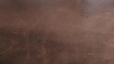 An image depicting a seamless transition or comparison on a dark brown, textured surface resembling leather or a rough material. A vertical blue line divides the image, with two small squares centered along it. The upper blue square features two opposing arrows, symbolizing exchange or change. The lower white square, labeled "Principle" and showing a hand icon with an index finger tapping a surface, suggests interaction or an explanation, possibly for a before-and-after view or the working mechanism of a technology.